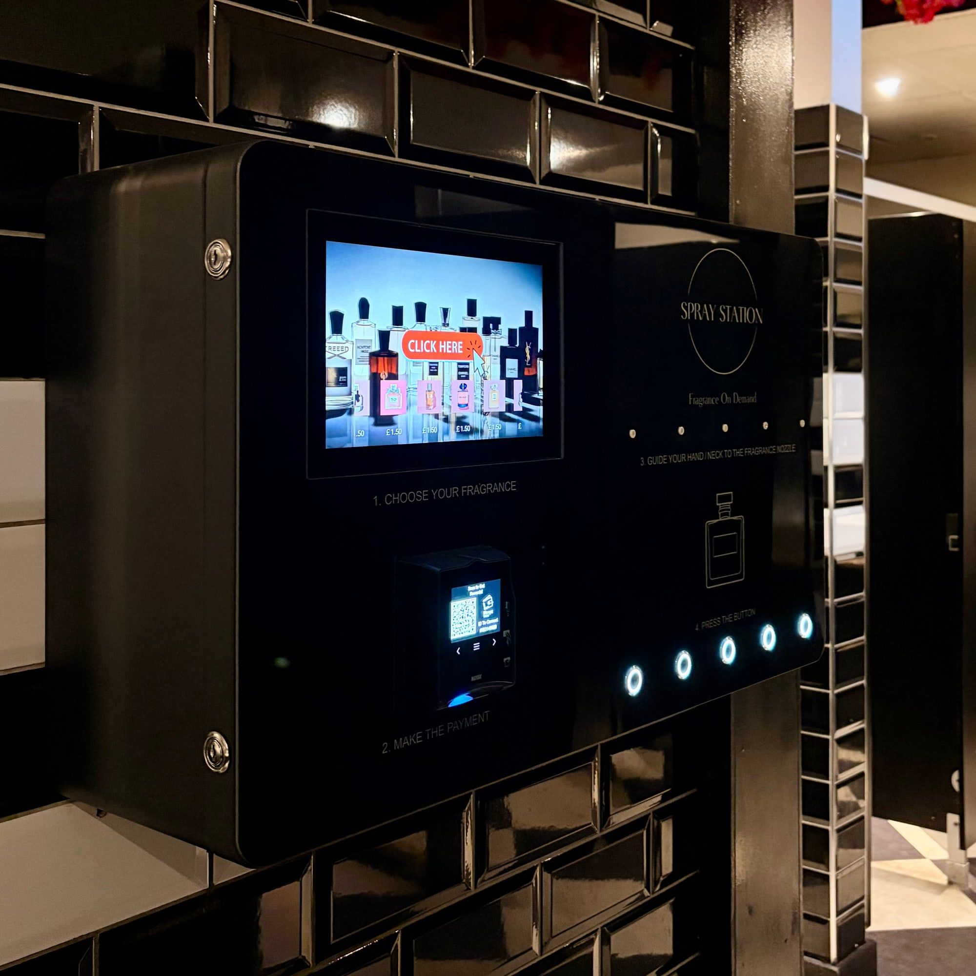 Spray Station wall-mounted perfume vending machine installed on a black-tiled venue wall